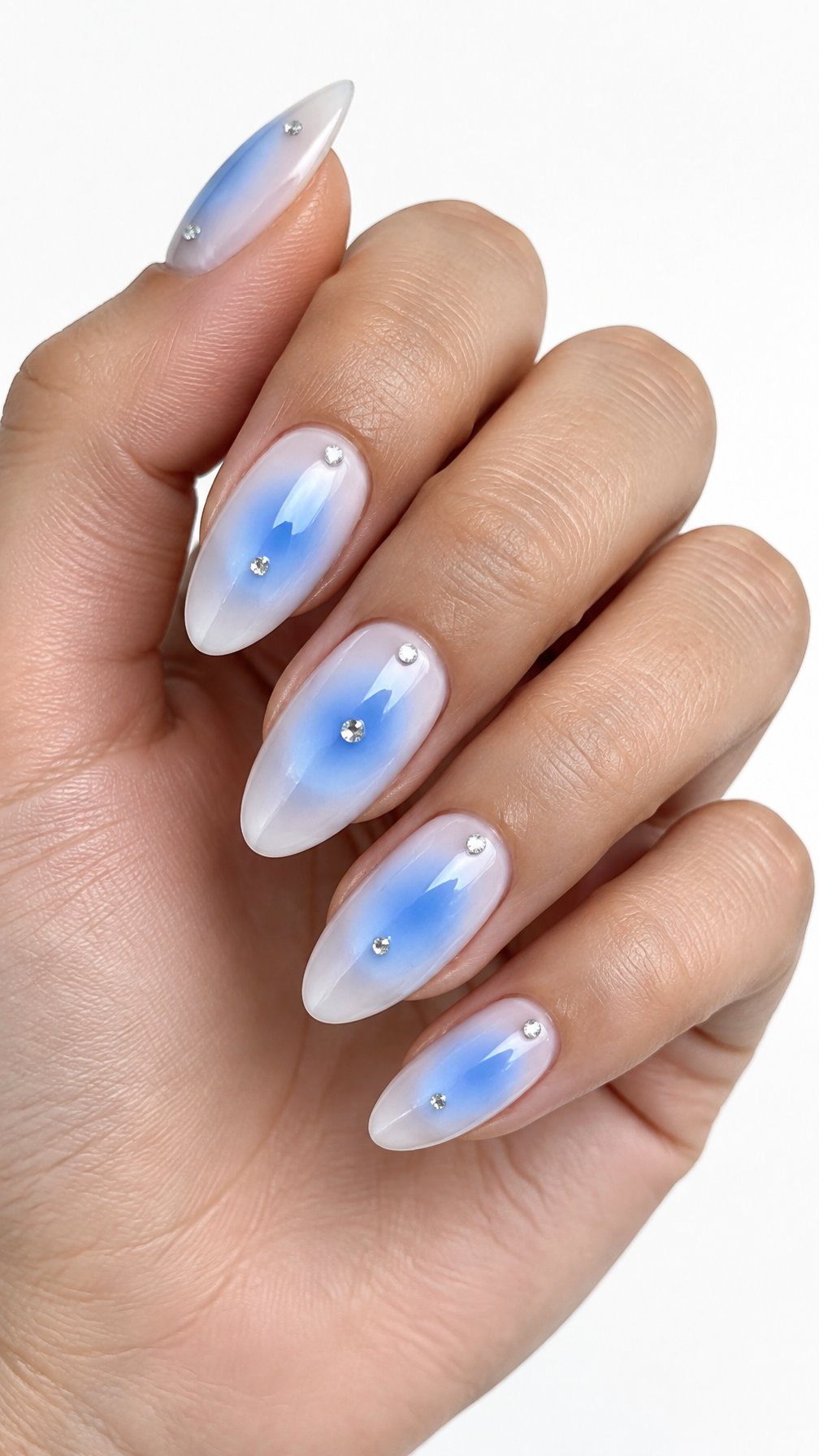 A single hand displays glossy sky-blue aura nails decorated with tiny gems against a white background.