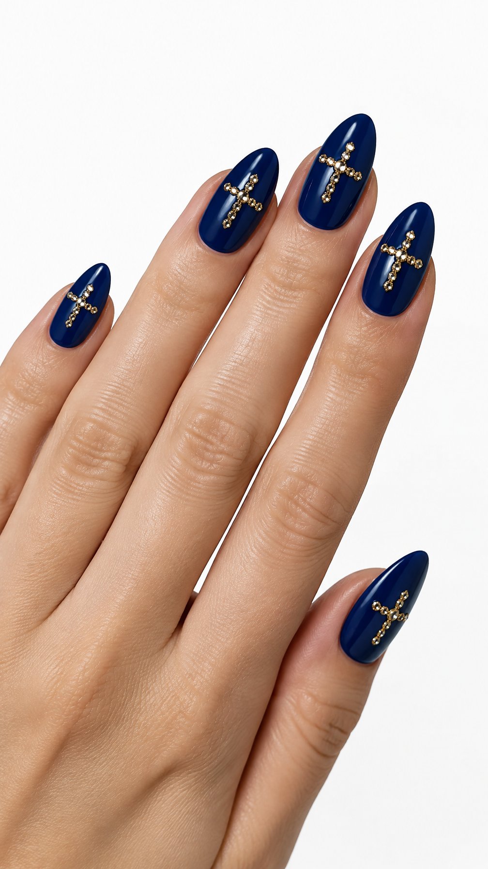 A single hand with glossy indigo-blue almond nails decorated with small gold rhinestone crosses against a white background.