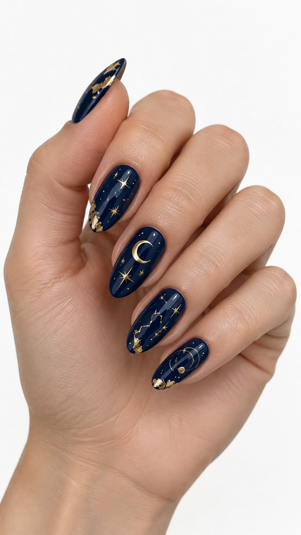 A single hand with almond-shaped navy blue nails decorated with gold stars, moons, and foil accents on a white background.