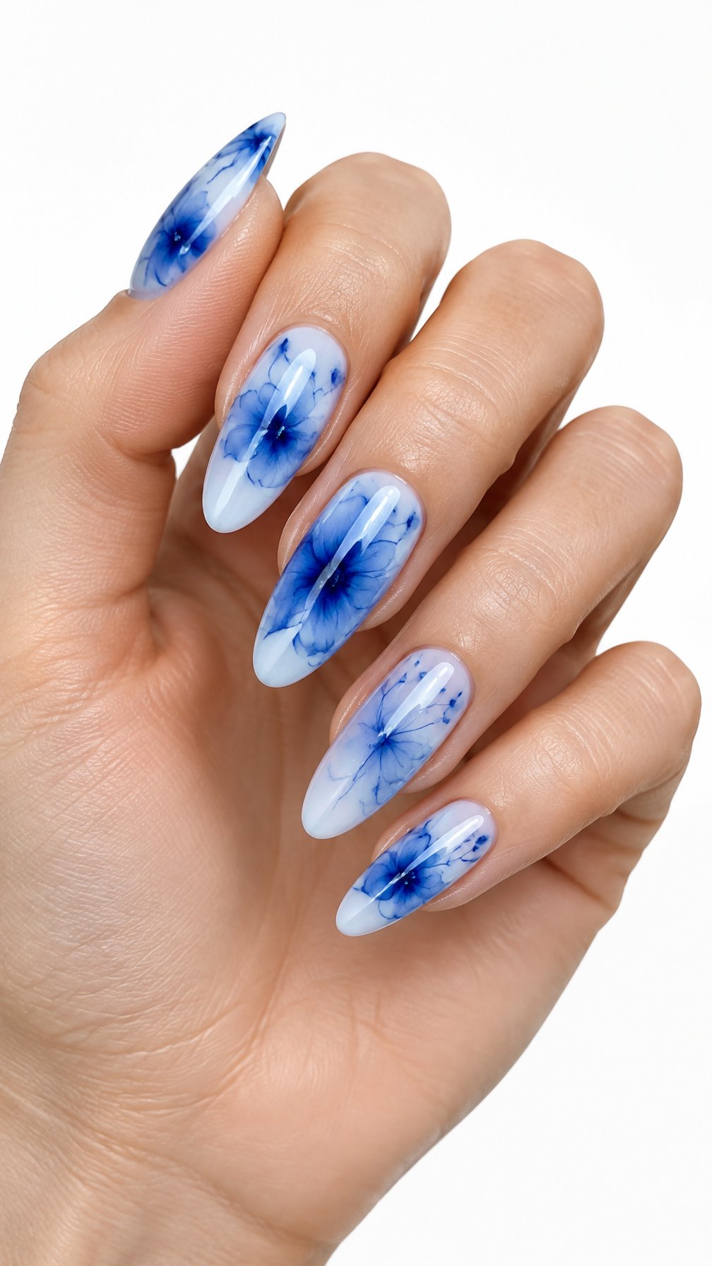 A single hand with long almond-shaped nails decorated with glossy indigo and blue floral designs on a white background.