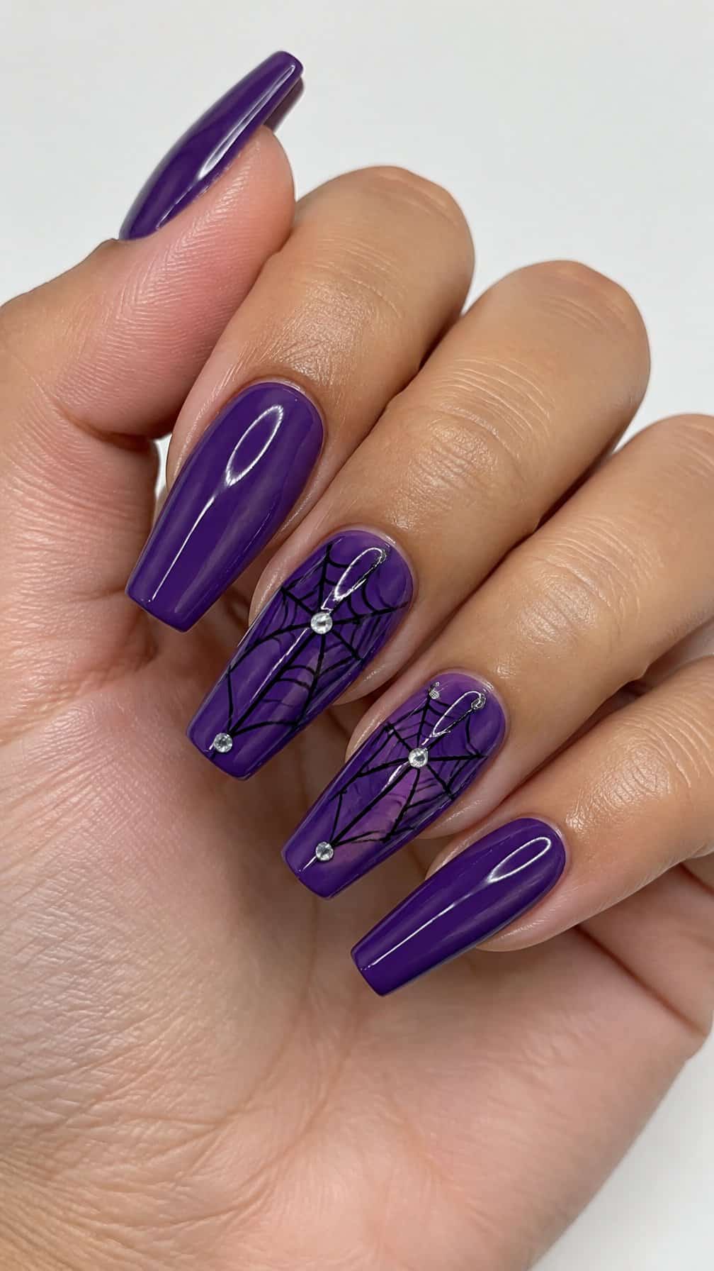 Glossy violet coffin-shaped nails, including solid purple nails and purple accent nails decorated with black spiderwebs and small rhinestones